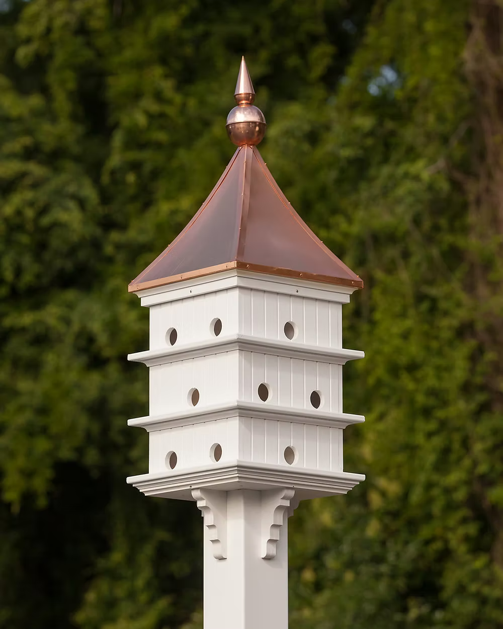 White birdhouse with a copper roof against a green foliage background